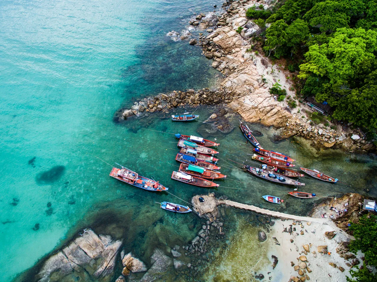 Aerial view of longtail boats on turquoise water along a rocky Thai coastline